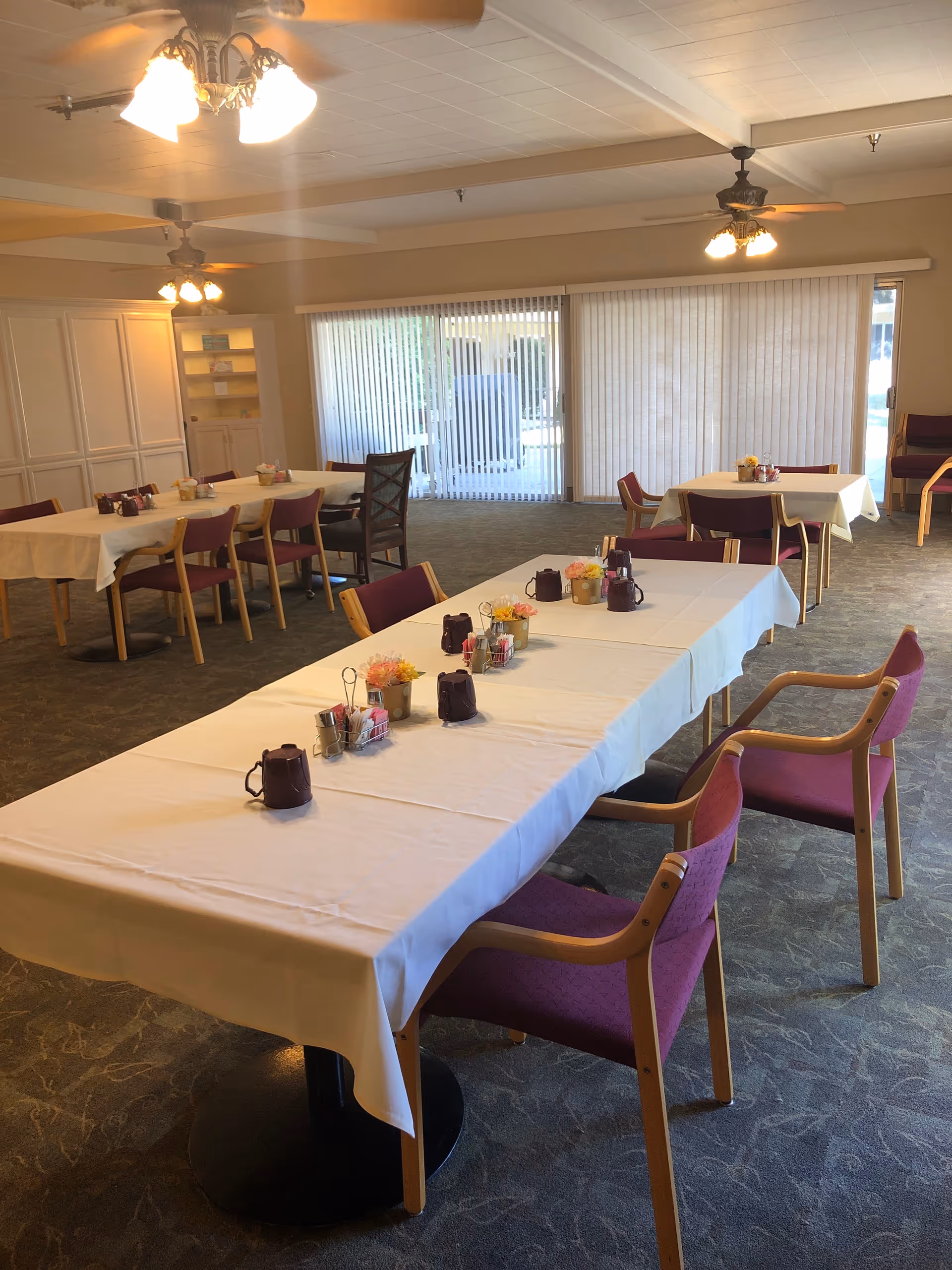 A bright dining room with white tablecloths, purple chairs, and sliding glass doors.