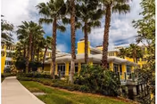 Exterior view of a yellow Cypress Cove senior living building with palm trees and a walkway.