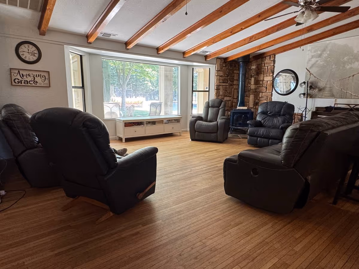 Cozy living room with recliners, stone fireplace, ceiling beams, and large window view.
