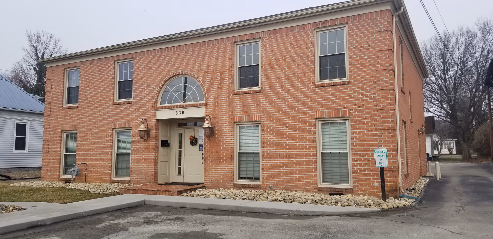 Brick two-story building with arched window above entrance and a landscaped front.