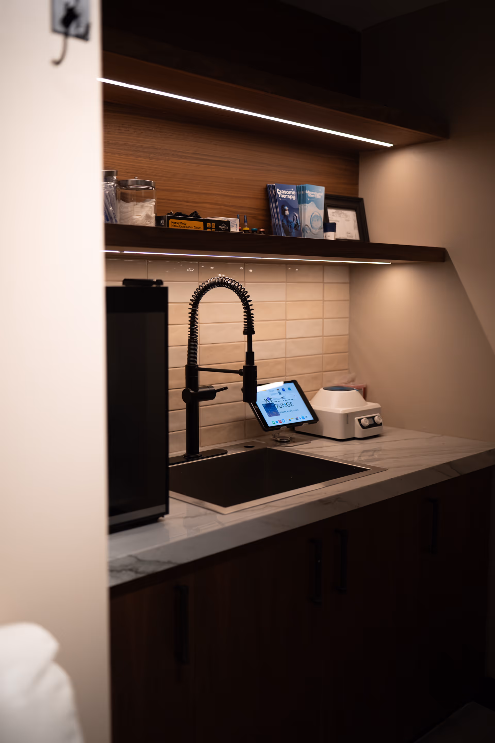 Modern kitchenette in a senior living facility with marble counter, black faucet, tablet, and appliances.