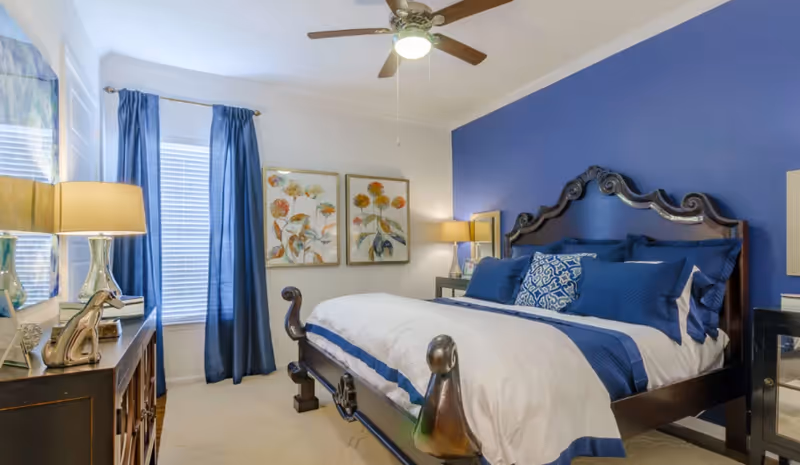 Winslow Commons bedroom featuring a blue-accent wall and ornate wooden bed.