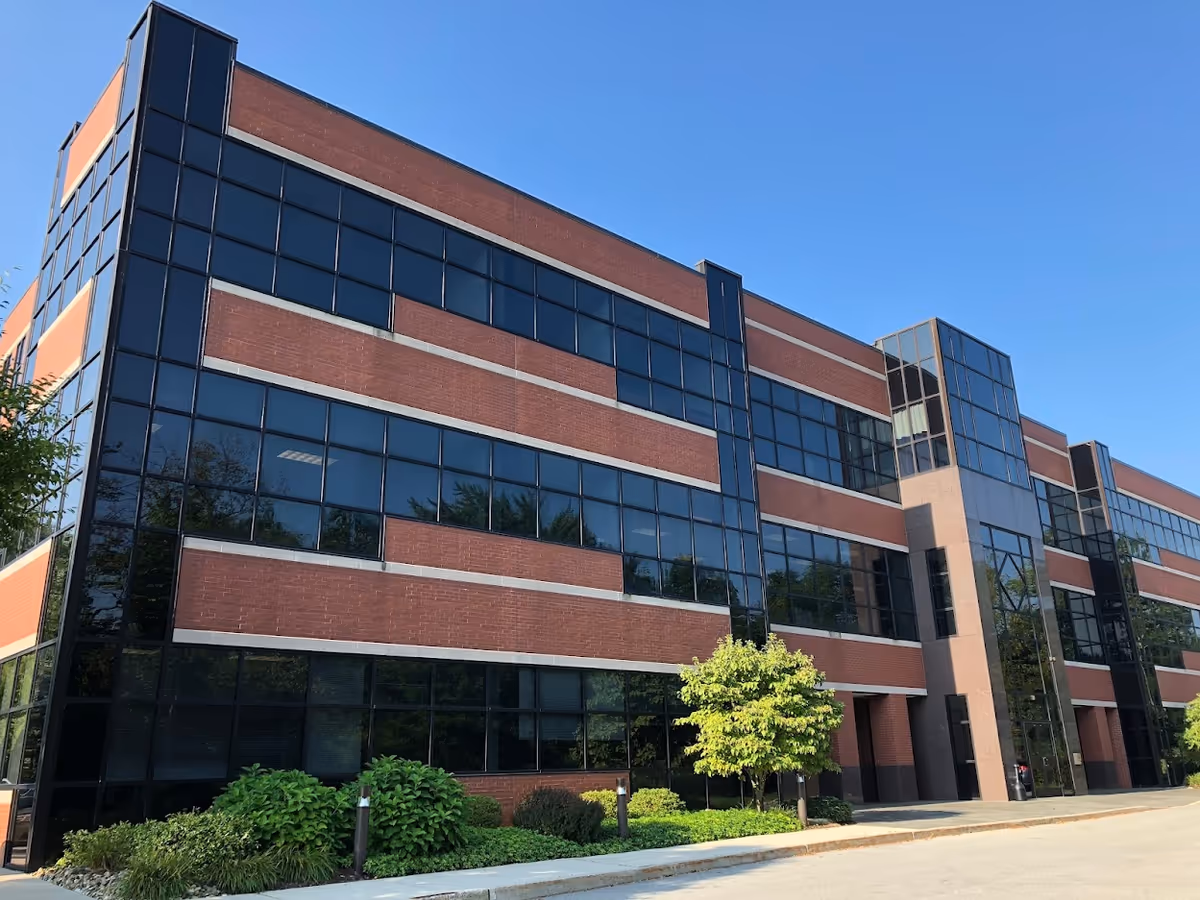 Modern brick-and-glass senior living facility exterior with landscaped shrubs and a clear blue sky.
