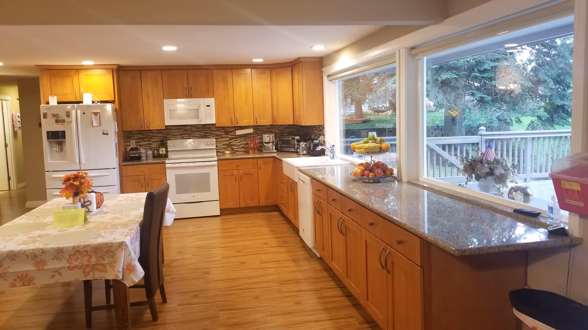 Bright kitchen with wooden cabinets, appliances, and a large window overlooking a backyard.