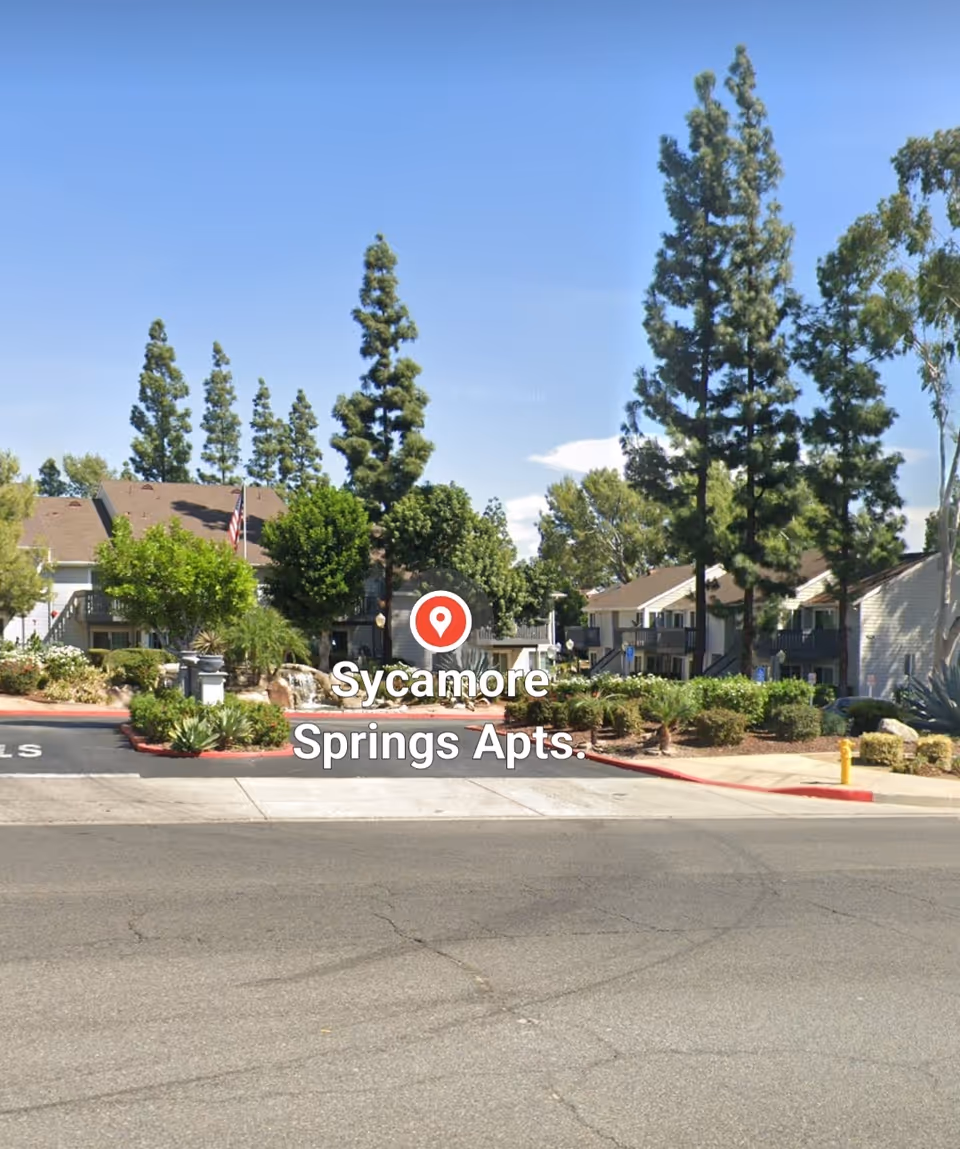 Front exterior of Sycamore Springs Apartments with trees and landscaping.