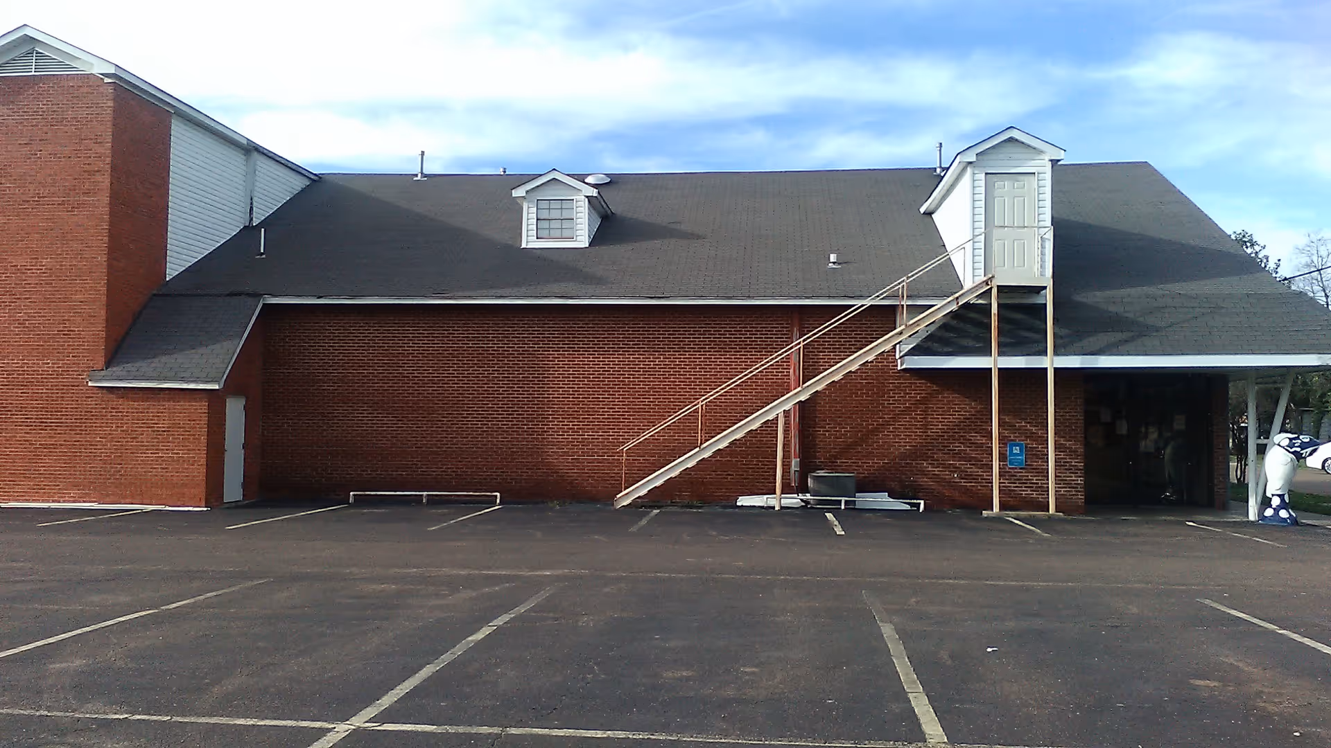 Exterior view of brick senior living facility with stairs to a second-floor entrance and parking area