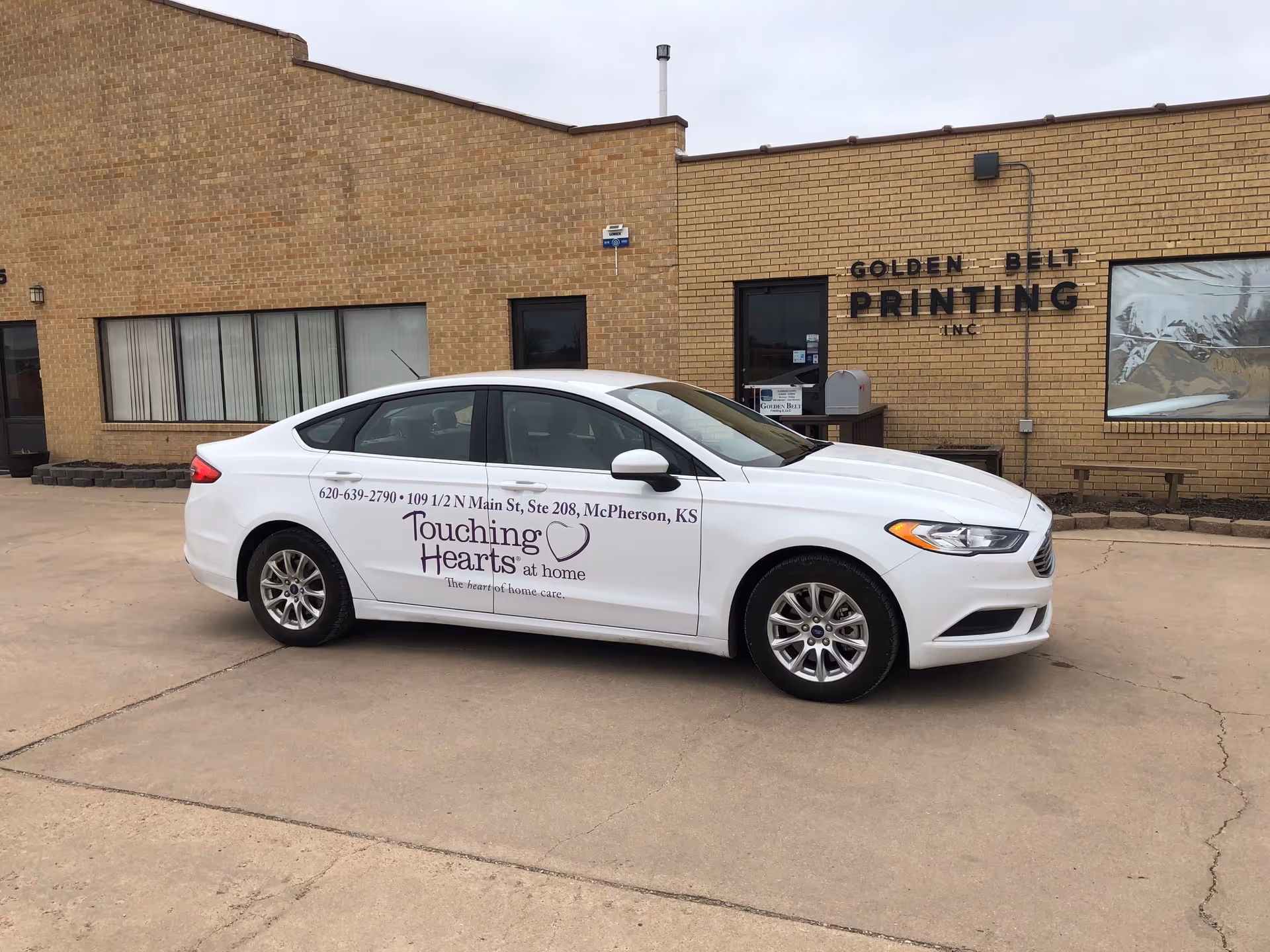 White car with Touching Hearts at Home branding parked in front of a brick building exterior