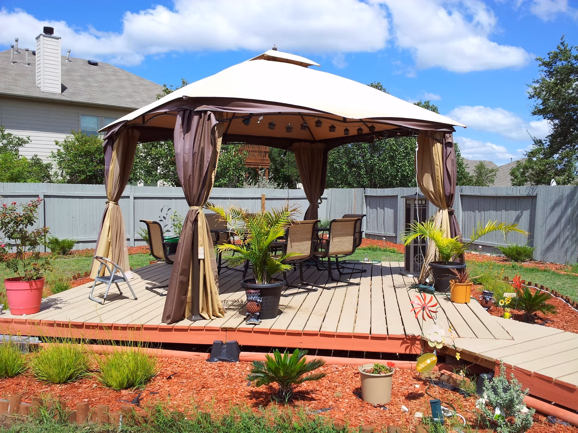 Outdoor gazebo with curtains and patio furniture on a wooden deck in a fenced yard.