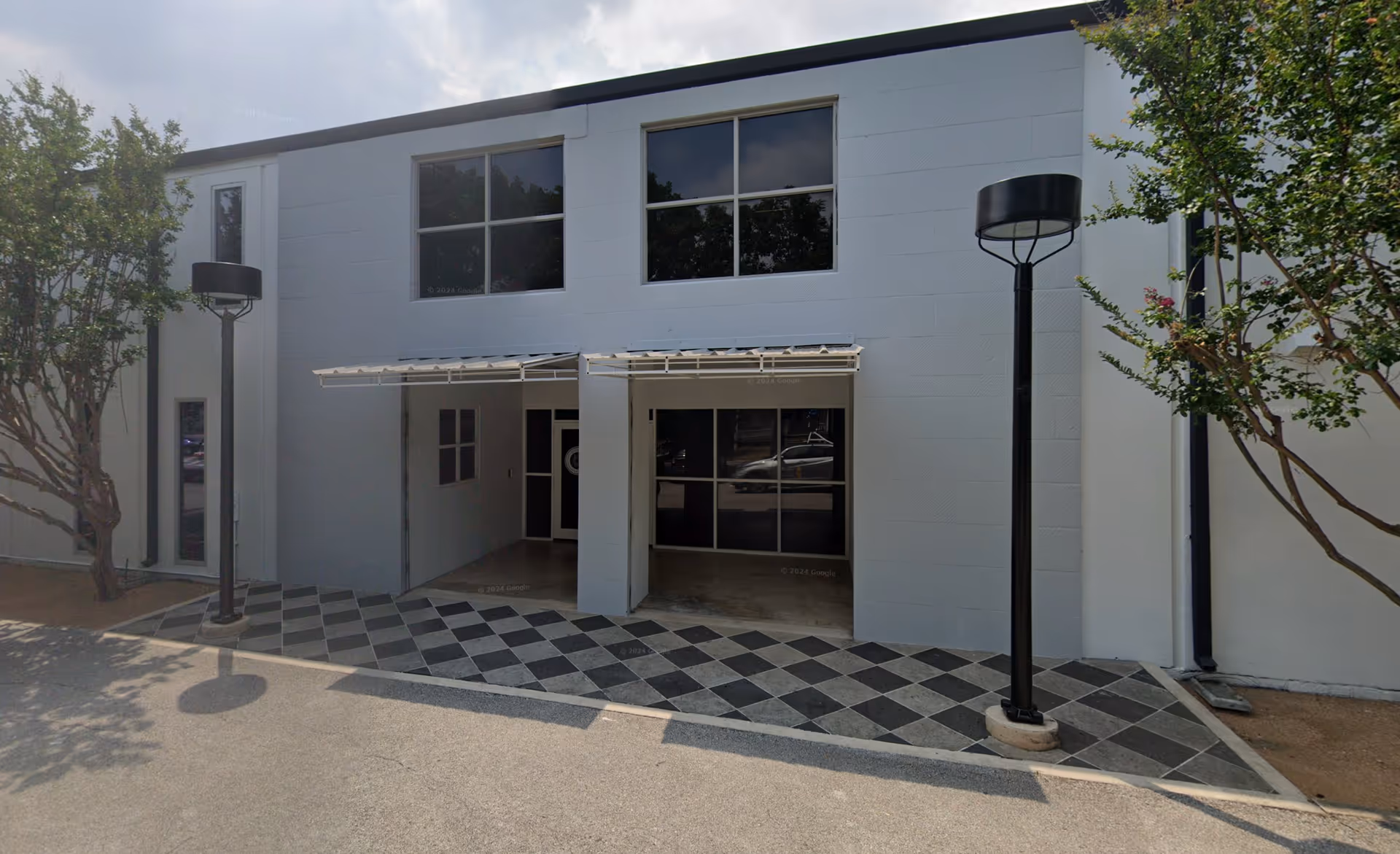 Exterior view of a modern building entrance with checkered tile walkway and trees.