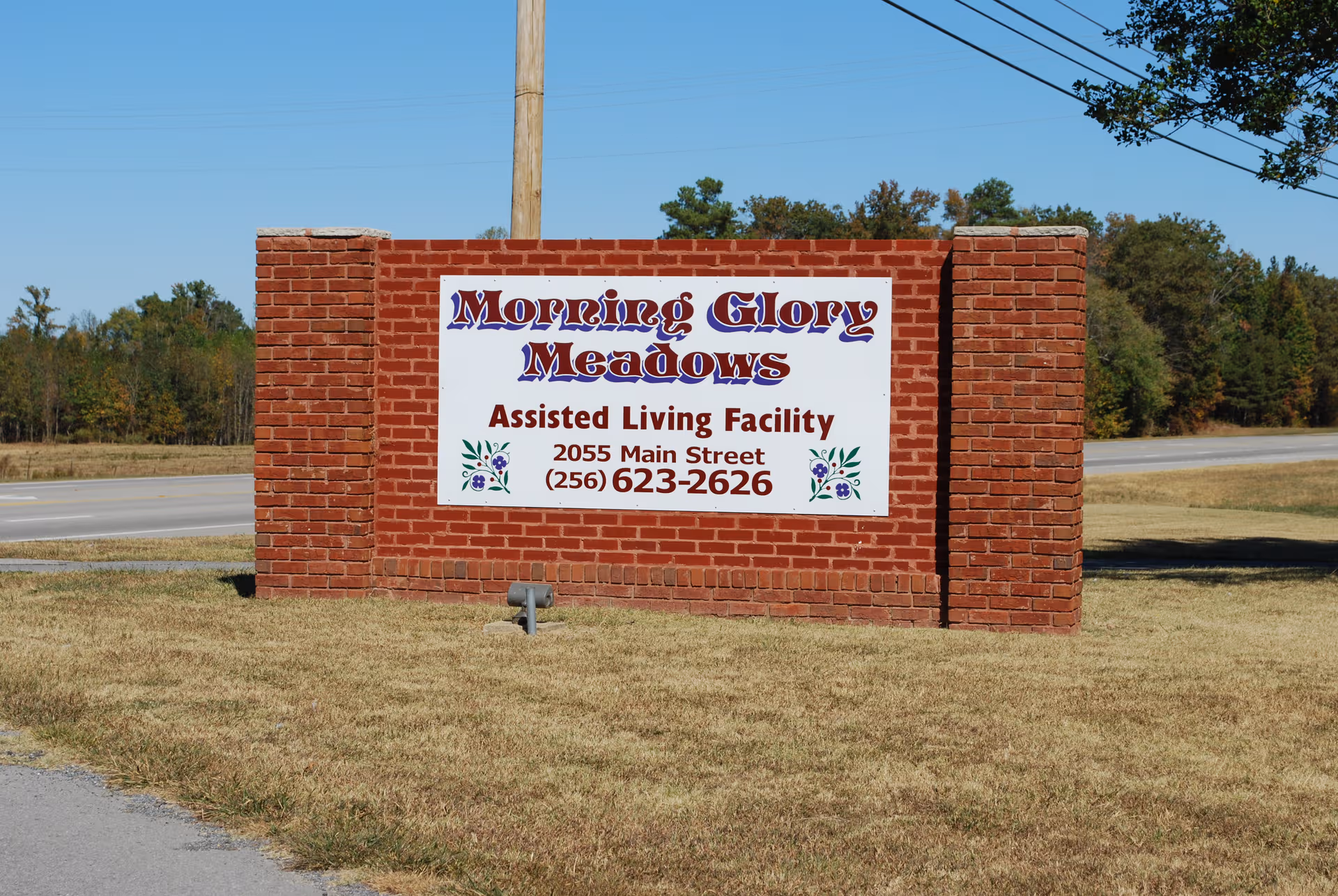 Brick sign for Morning Glory Meadows Assisted Living Facility beside a road.
