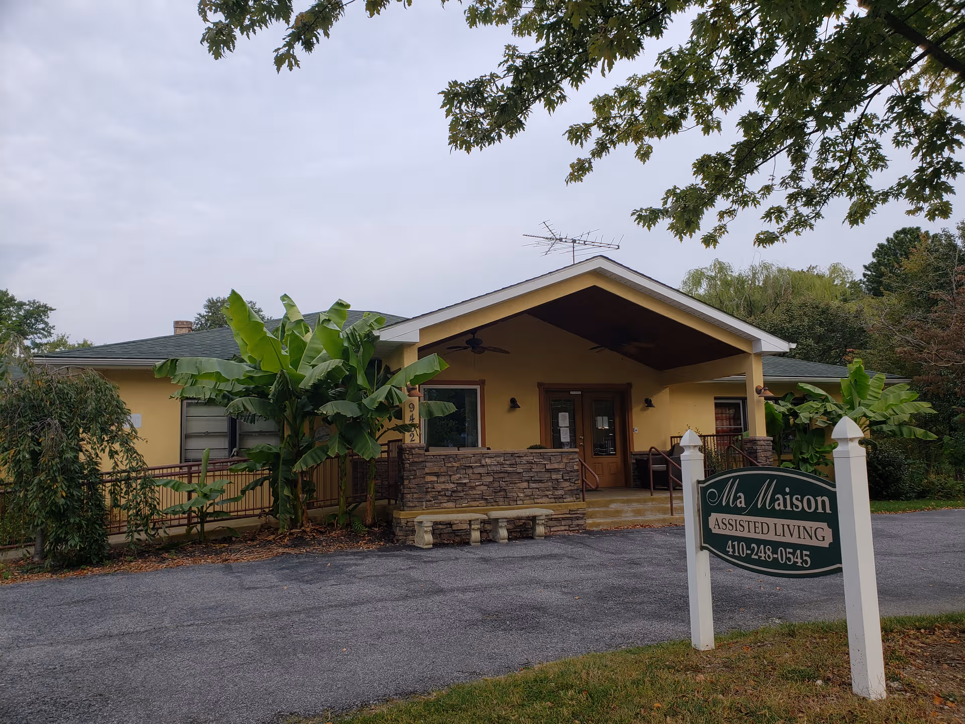 Front view of Ma Maison Assisted Living facility with sign, entry porch, and tropical plants.