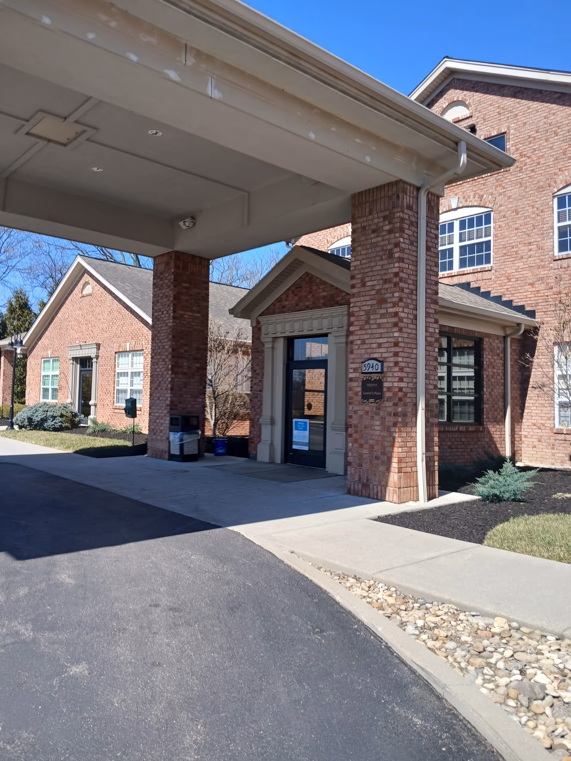 Brick hospice building entrance with covered driveway under a bright blue sky.