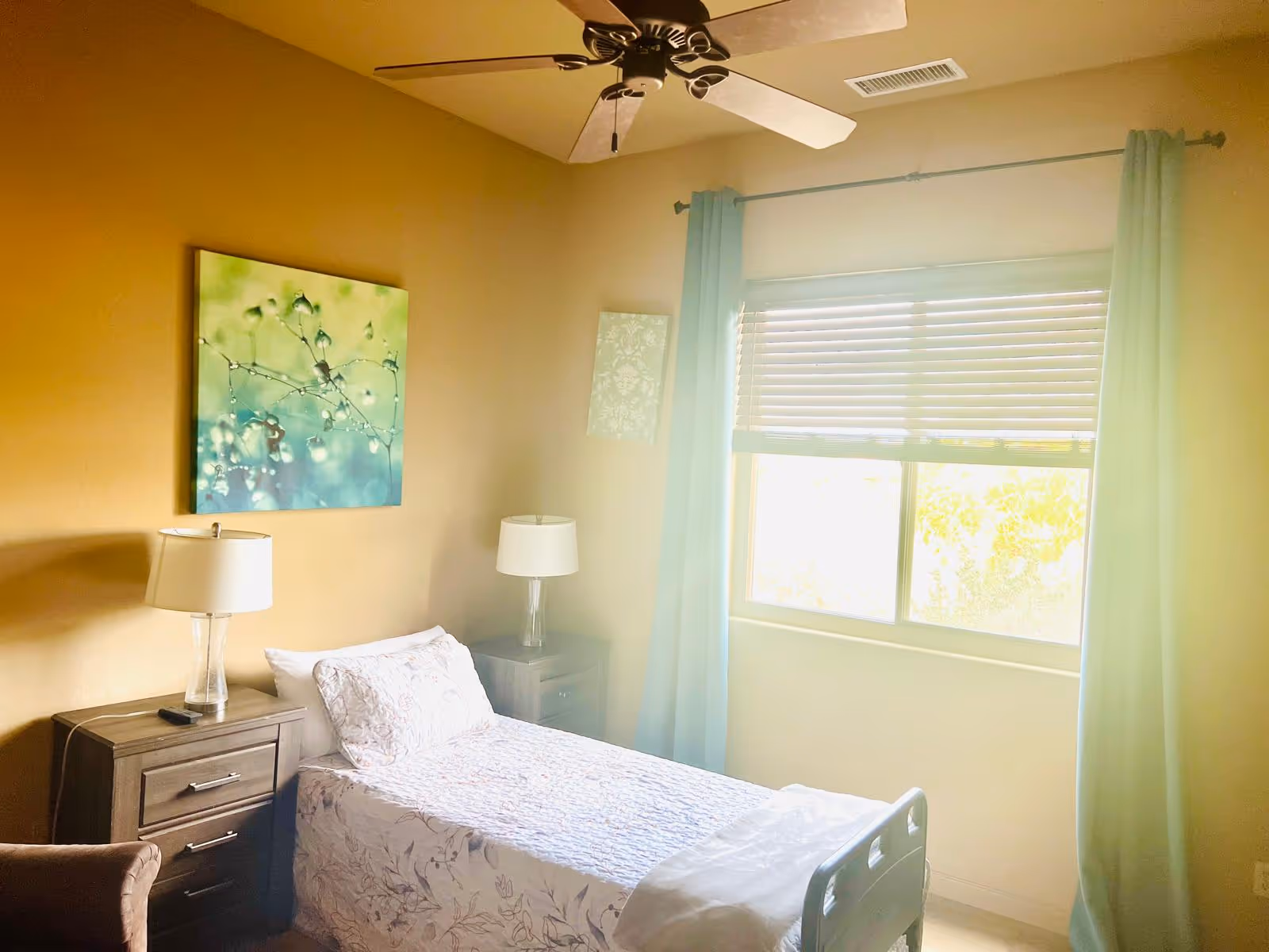 Cozy bedroom in a senior living facility featuring a bed, two nightstands, and window with curtains.