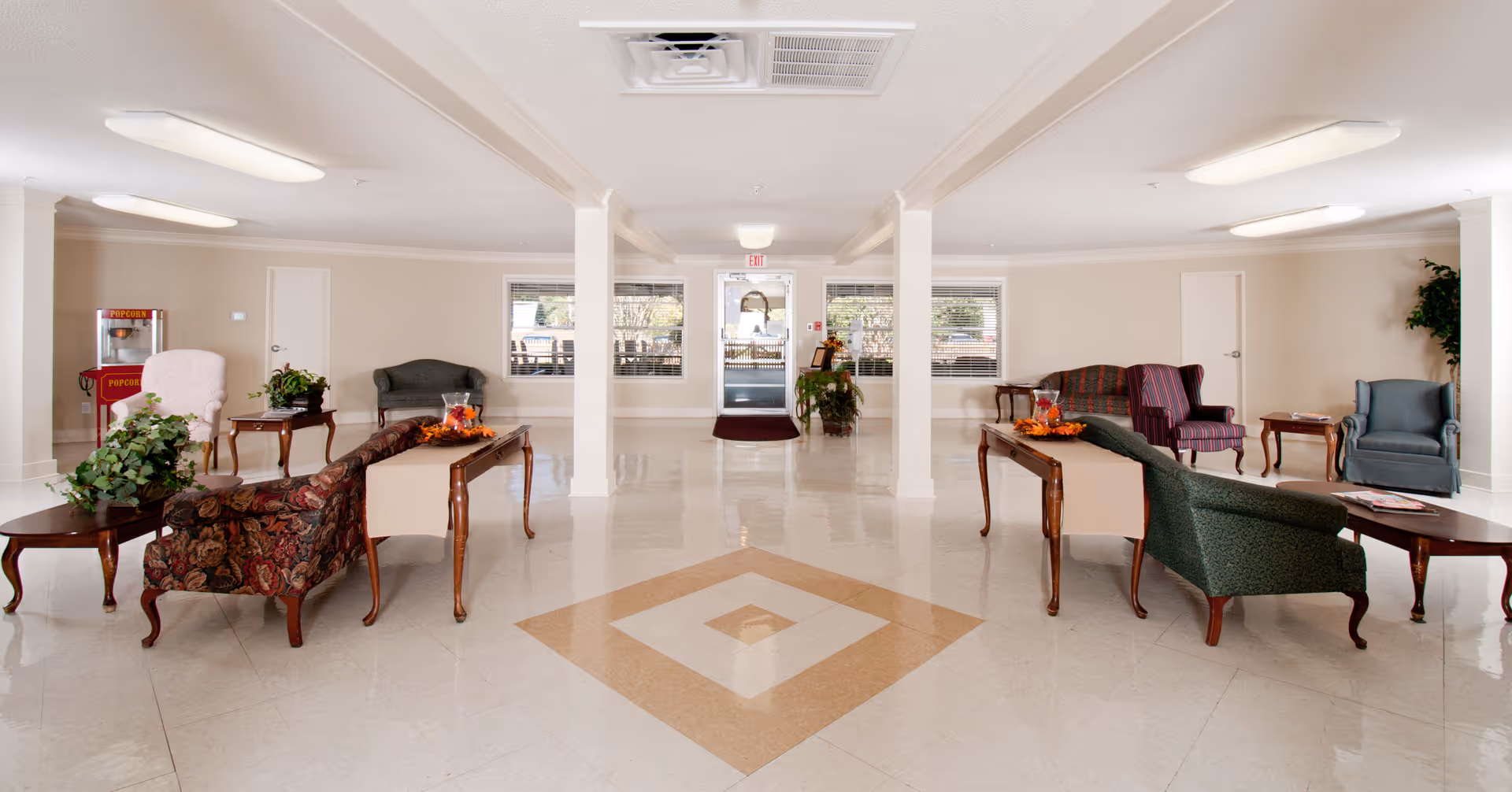 Spacious lobby with couches, chairs, and a central diamond-pattern floor in a senior living facility.