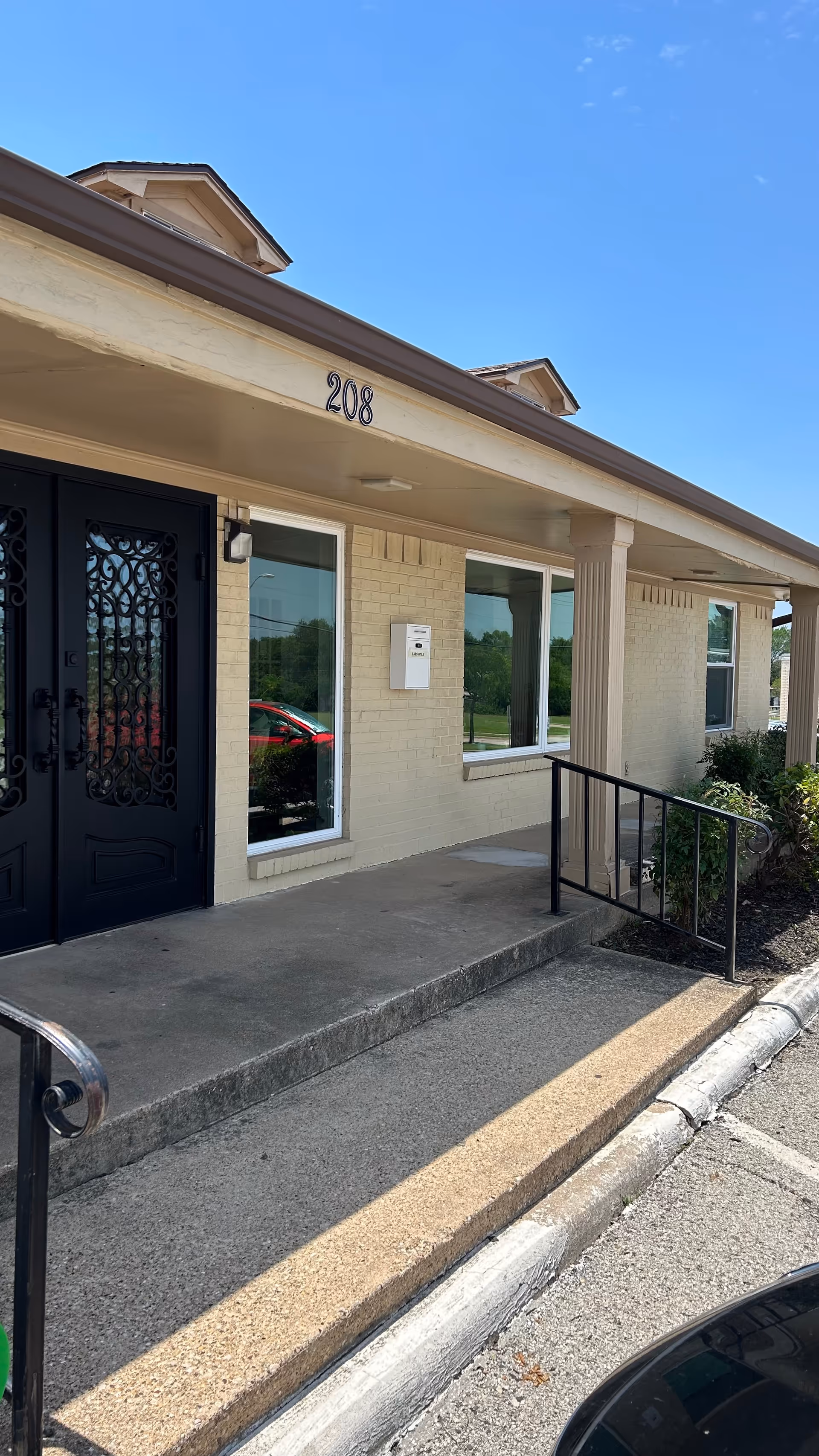 Exterior view of a beige facility entrance with a black ornate door.