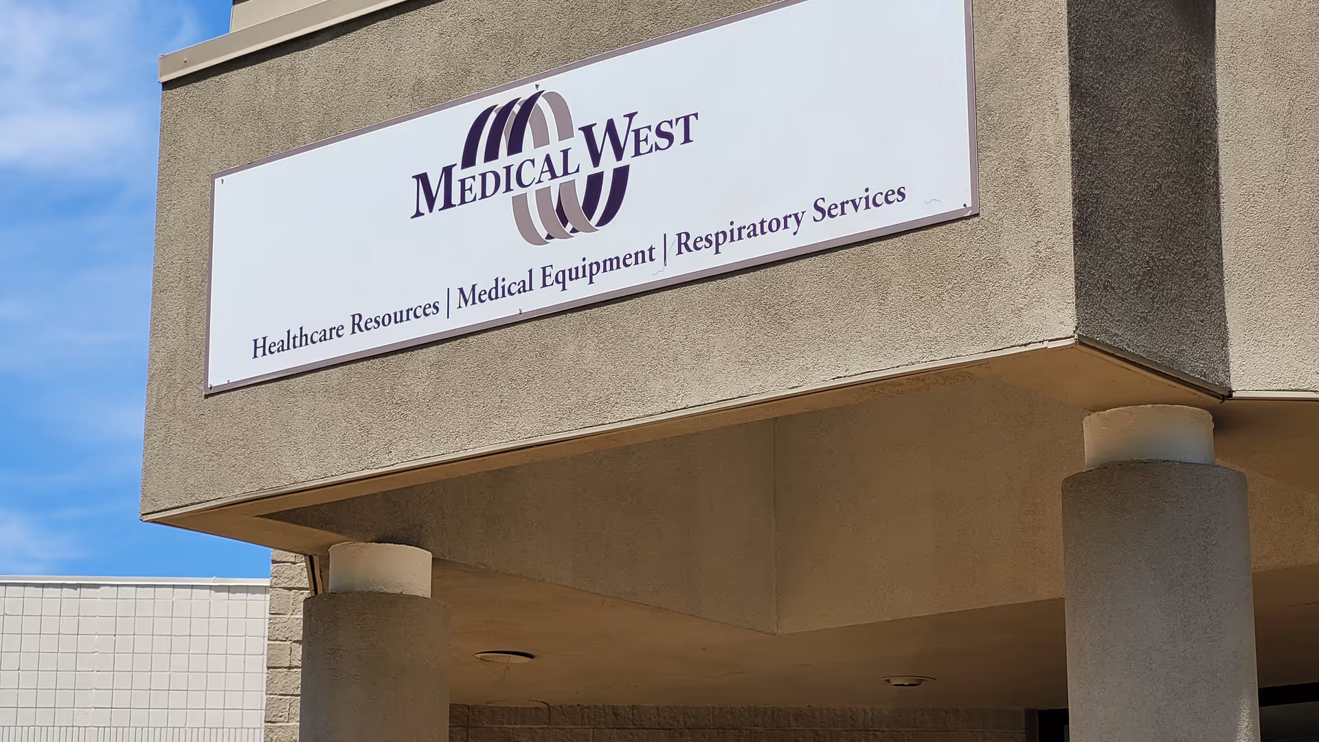 This is the front exterior of Medical West building with a sign and pillars.