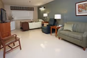 Interior senior living suite featuring a bed, sofa, chairs, and lamps.