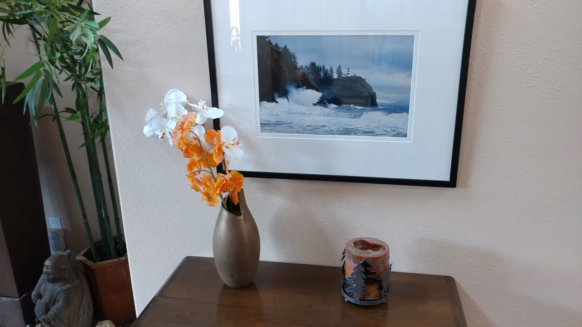 Decorative interior scene with framed ocean photo, vase of flowers, candle, and plant.