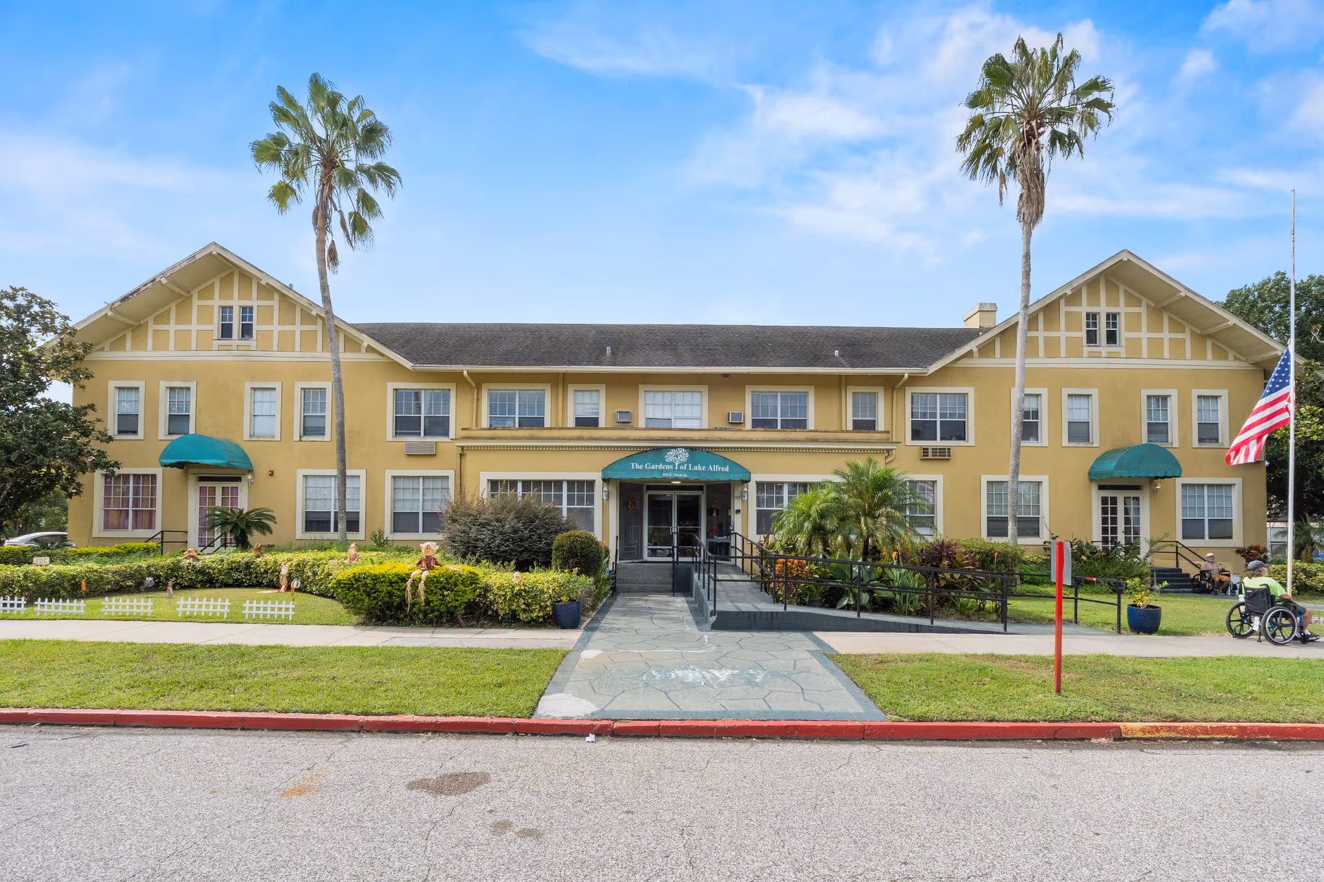Two-story yellow senior living building with palm trees and a central entrance.
