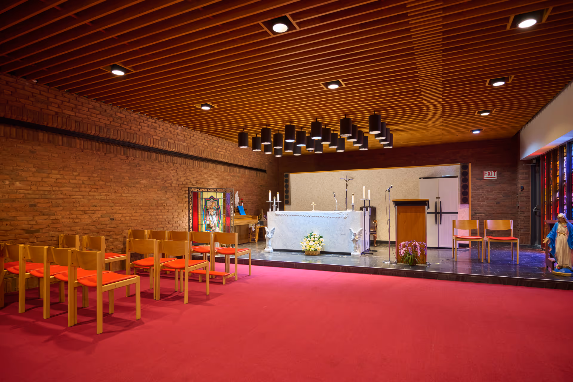 Interior chapel area with altar, lectern, candles, statues, and rows of wooden chairs.