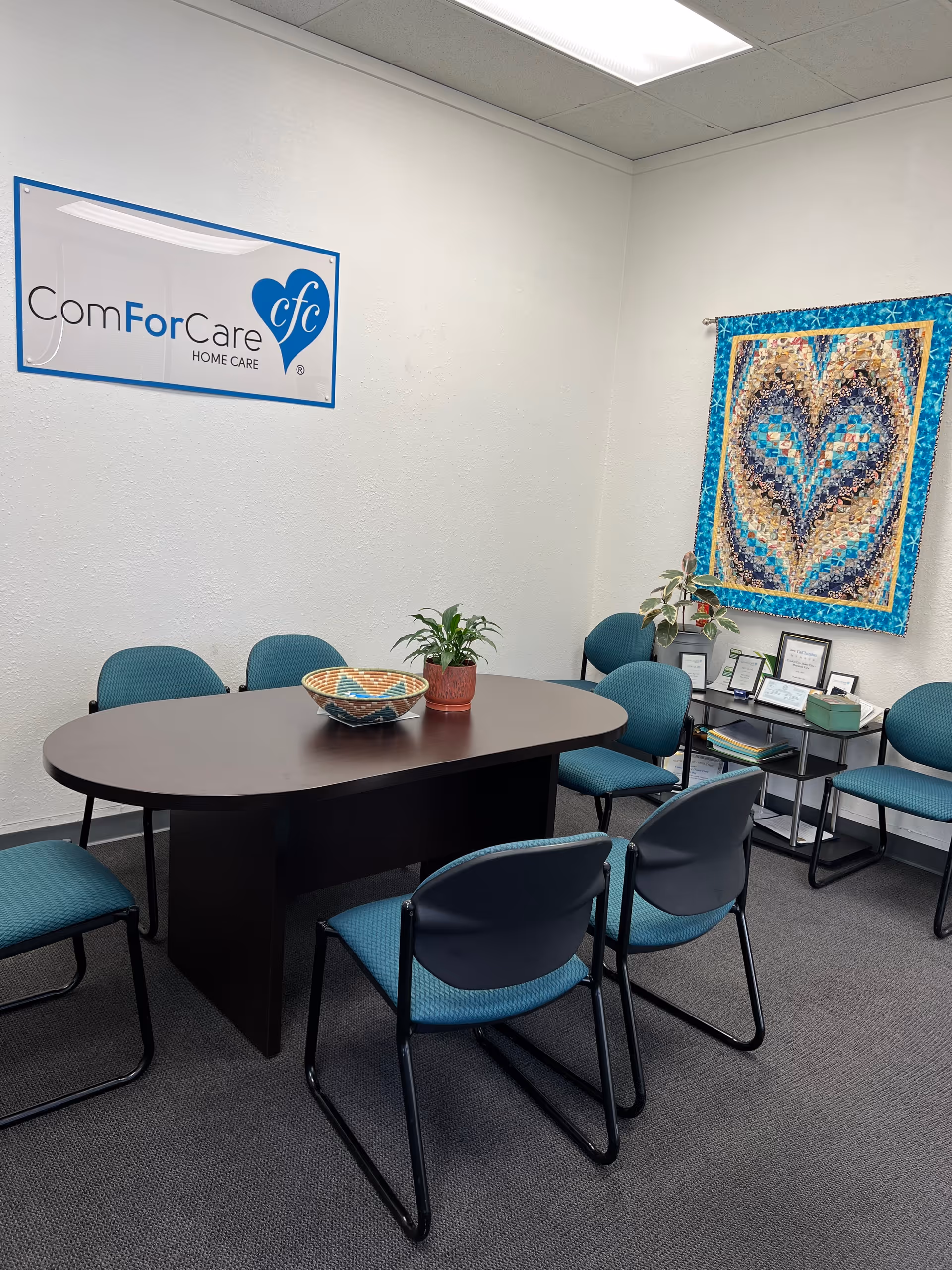 Interior meeting room with a round table, blue chairs, and a ComForCare sign on the wall.