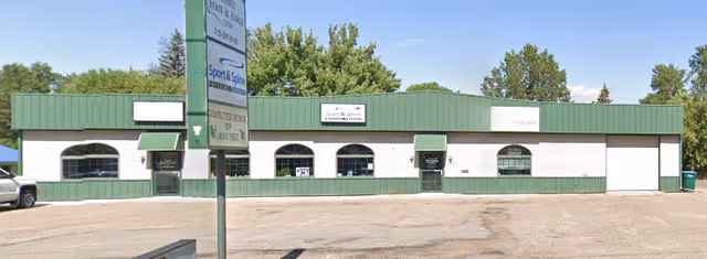 Front exterior of a single-story green-and-white commercial building with a parking lot.