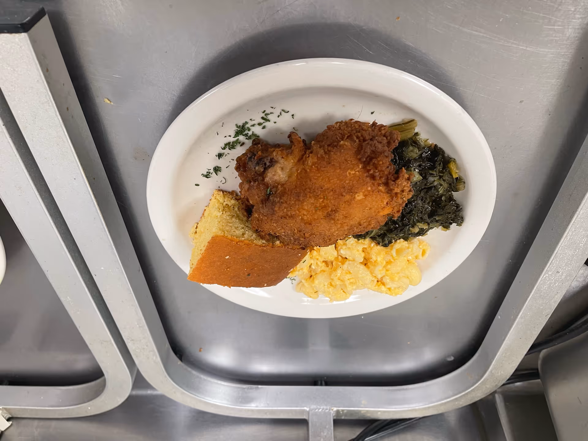 Plate with fried chicken, greens, bread, and scrambled eggs on a metal tray.