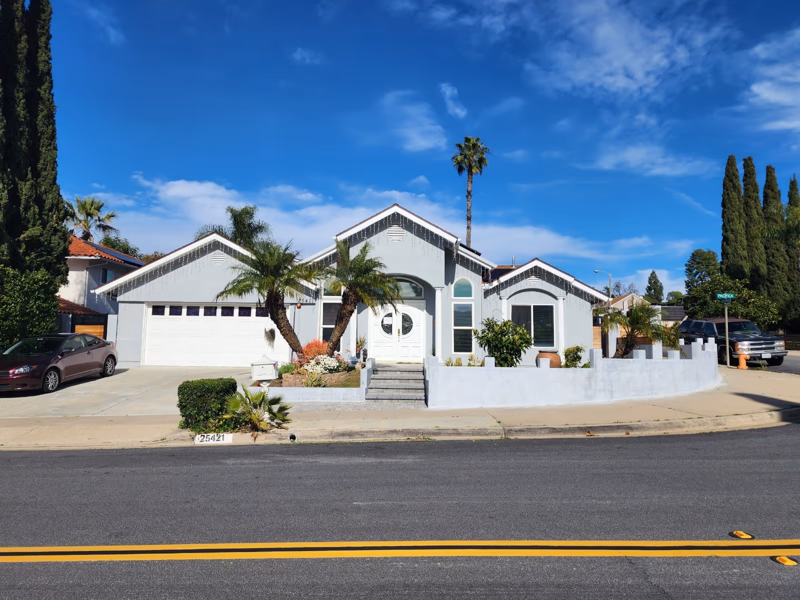 A single-story light-blue building with palm trees and a curved front yard.