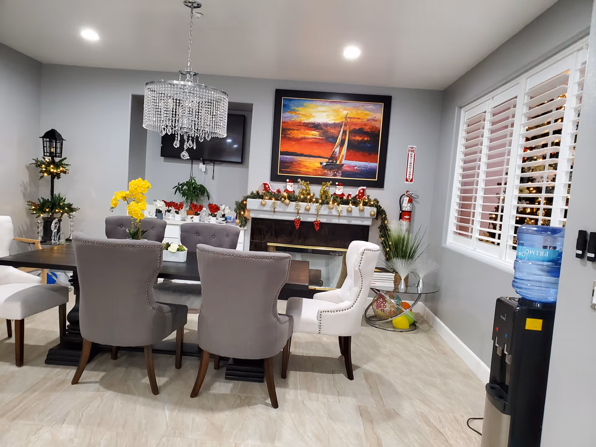 Dining room with chandelier, fireplace, garland, and gray upholstered chairs around a dark table
