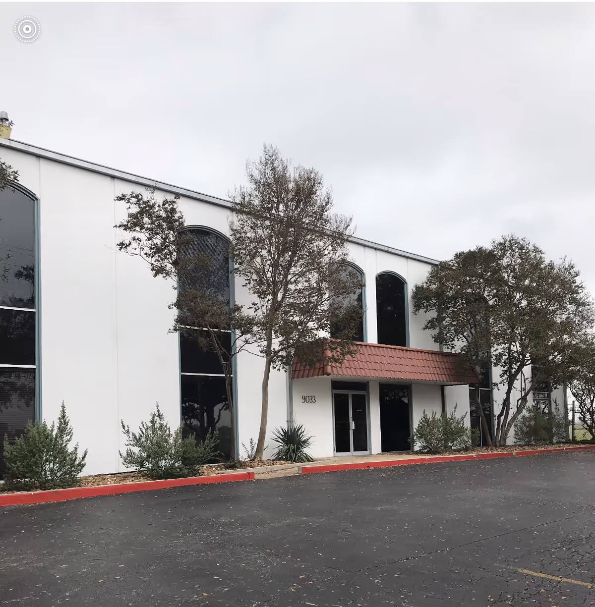White modern senior living facility exterior with arched windows and a red entrance canopy.