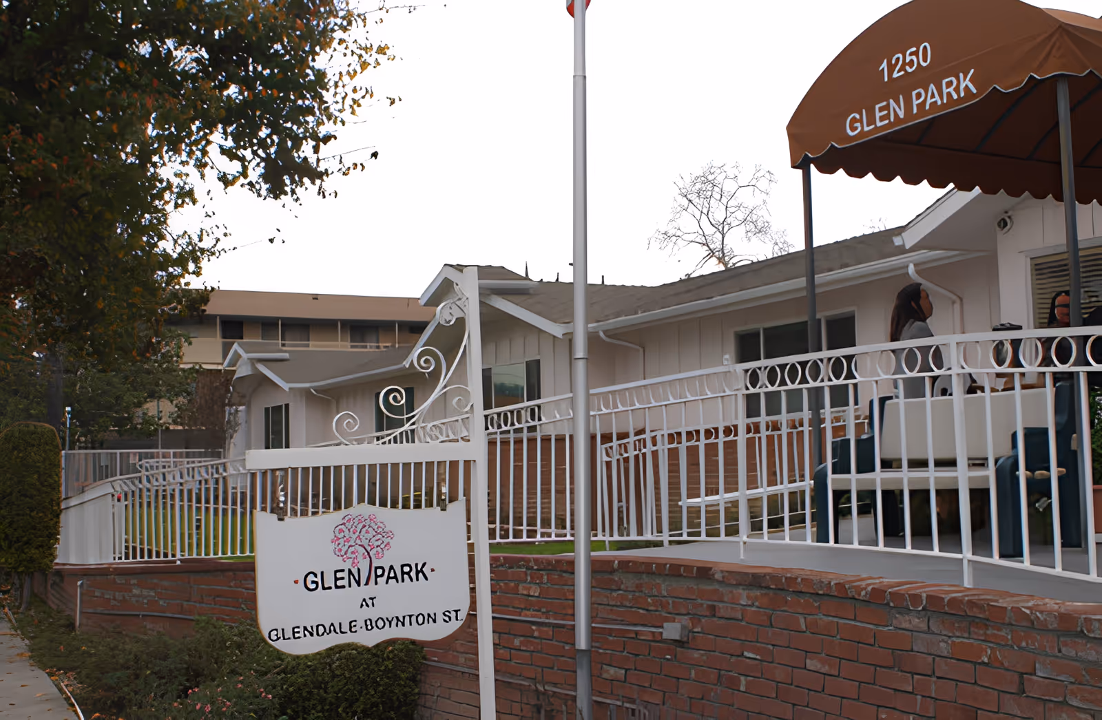 Front entrance of Glen Park senior living facility showing a sign, brick wall, white railing and an awning with the address.