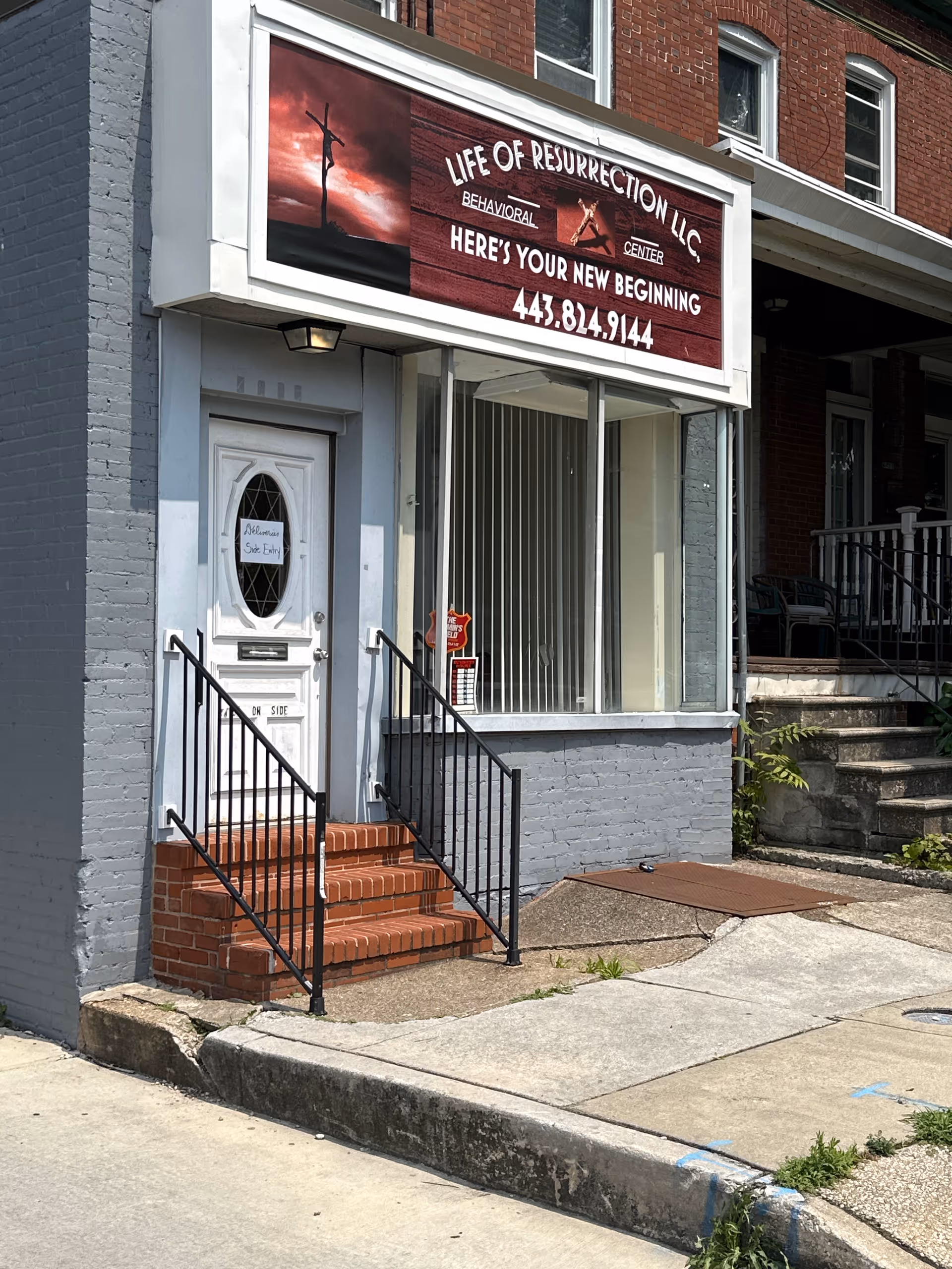 Exterior storefront of Life of Resurrection facility with sign, door, and brick steps.