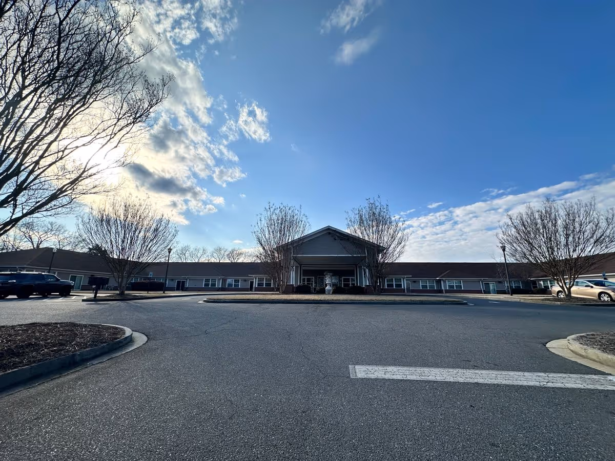 Wide, low-angle view of TerraBella Rock Hill's single-story building and main entrance with a circular driveway and leafless trees under a blue sky.