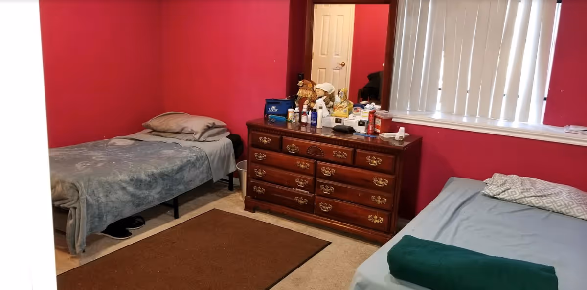 Two twin beds flank a wooden dresser in a pink-walled shared bedroom.