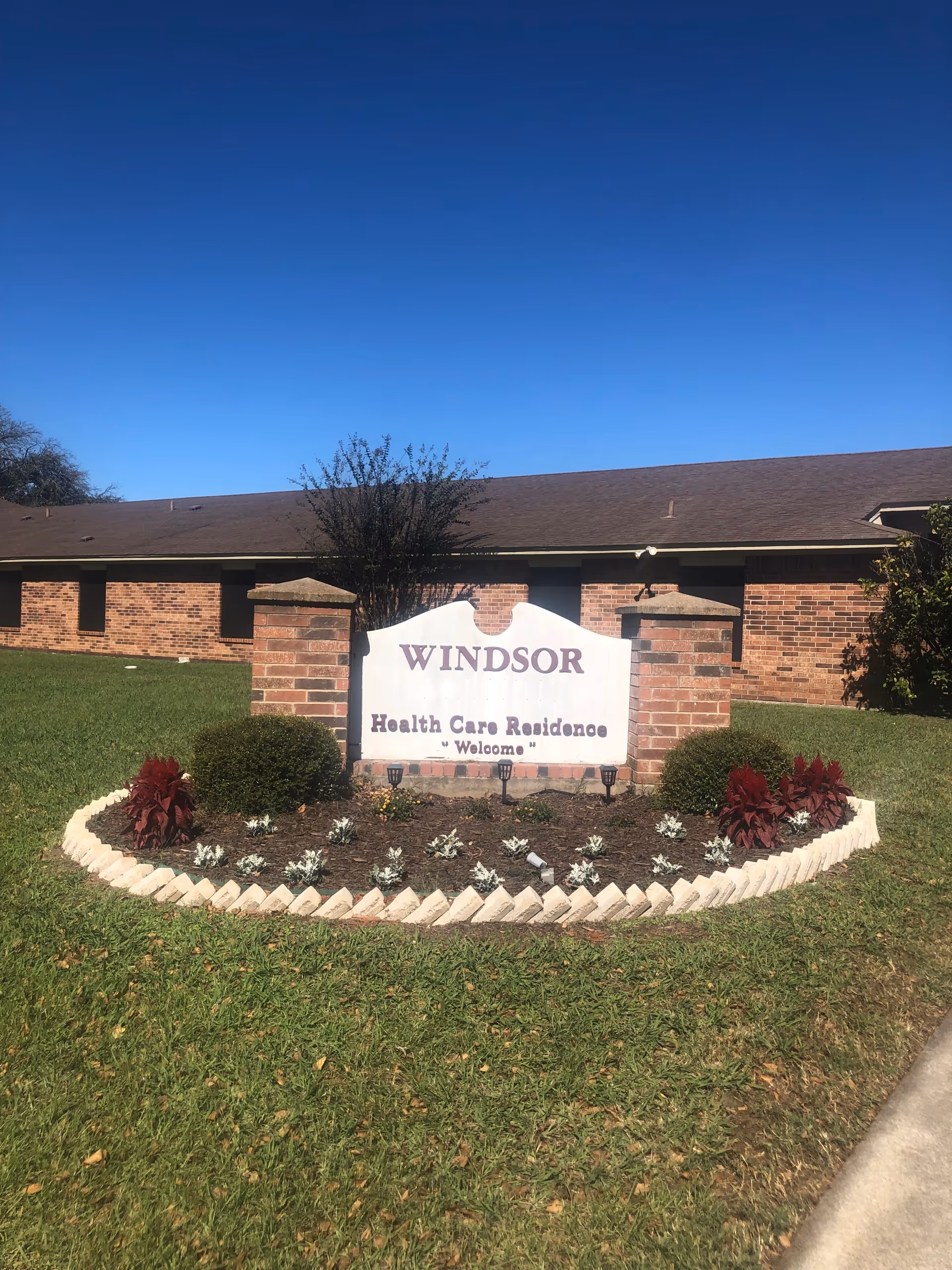Exterior view of Windsor Health Care Residence sign with brick building and landscaped front yard.