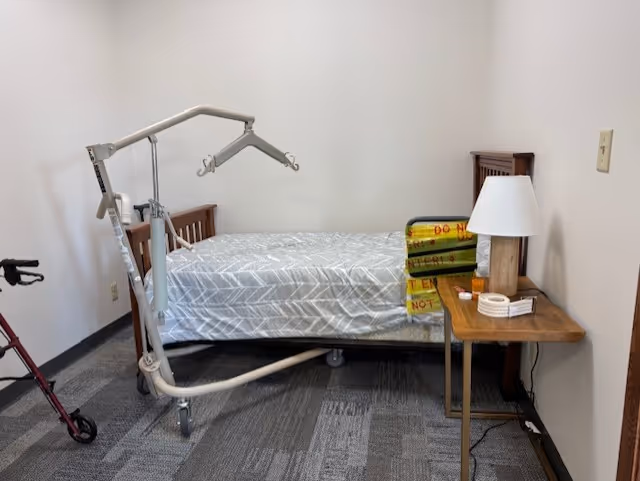 Small bedroom with a bed, patient lift, walker, and nightstand.