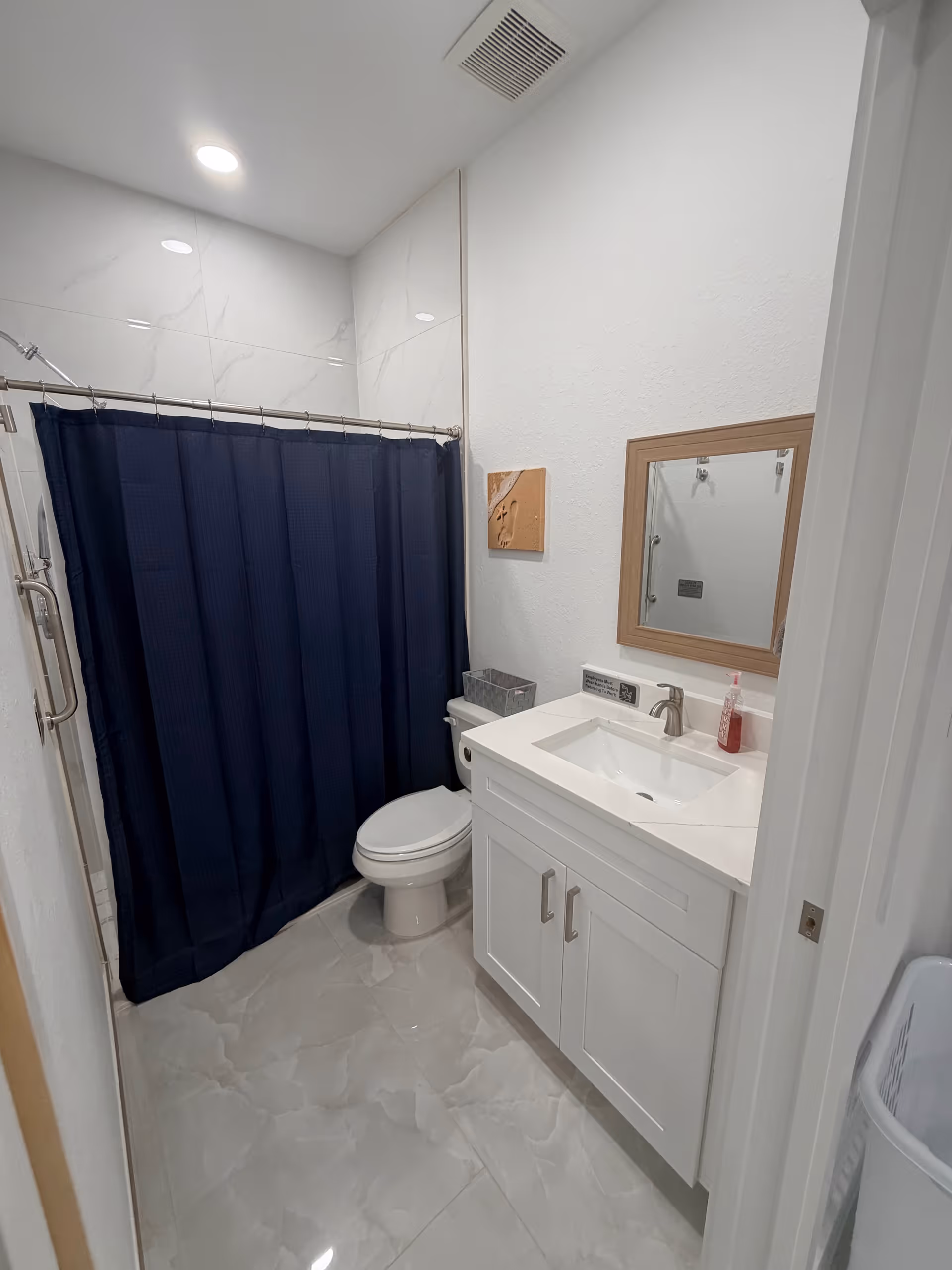 Small modern bathroom in senior facility with white vanity, toilet, and navy shower curtain.