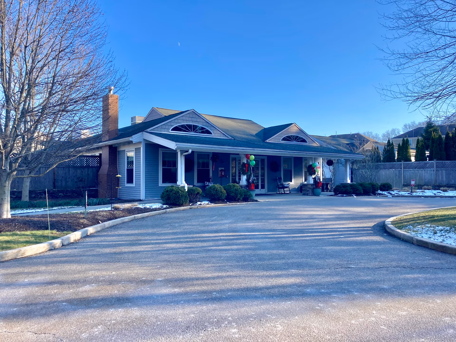 Single-story building front with a covered entrance, driveway, and landscaping under a clear blue sky.