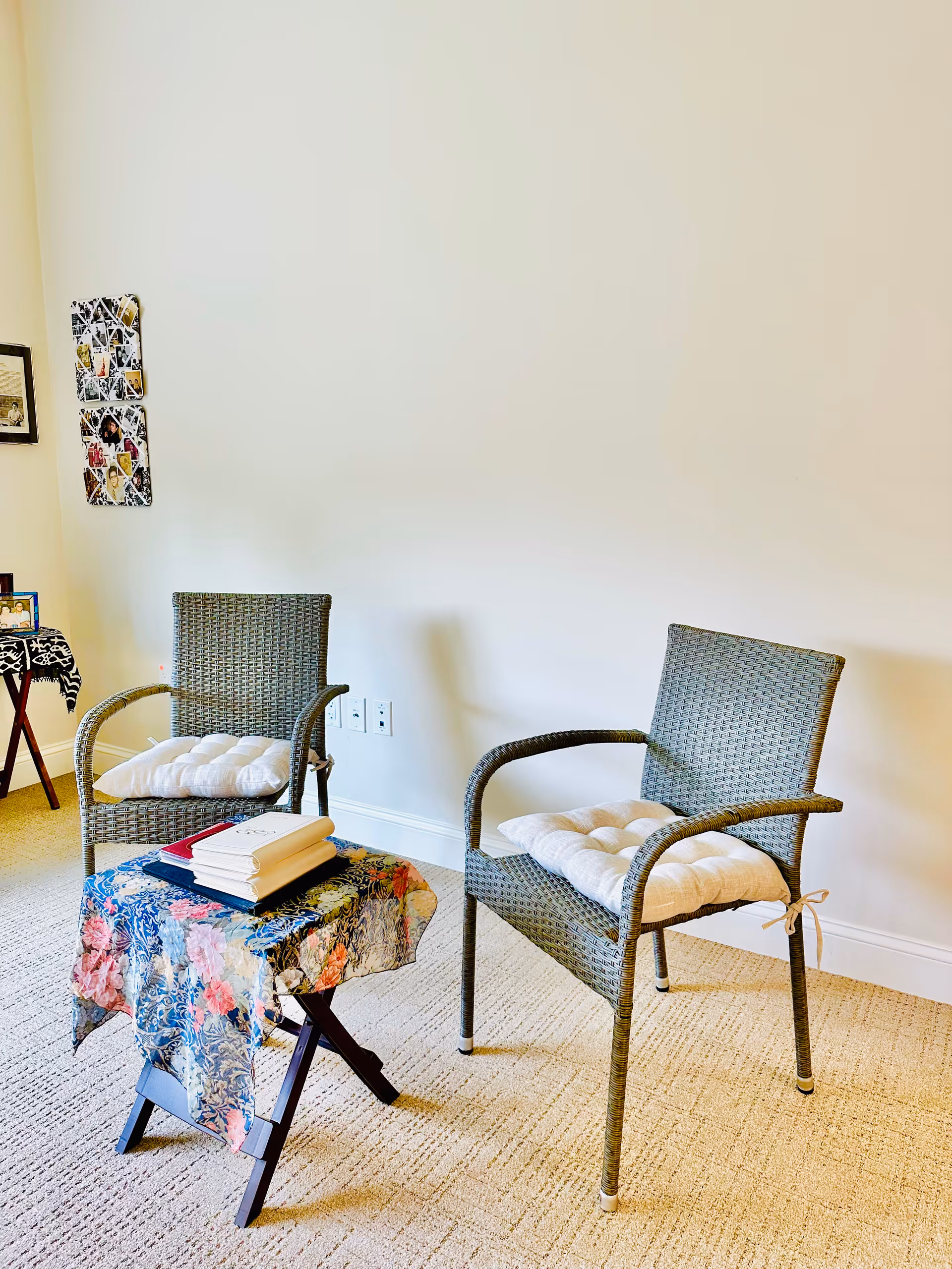 Two wicker chairs with cushions sit beside a small, cloth-covered table in a quiet living lounge.