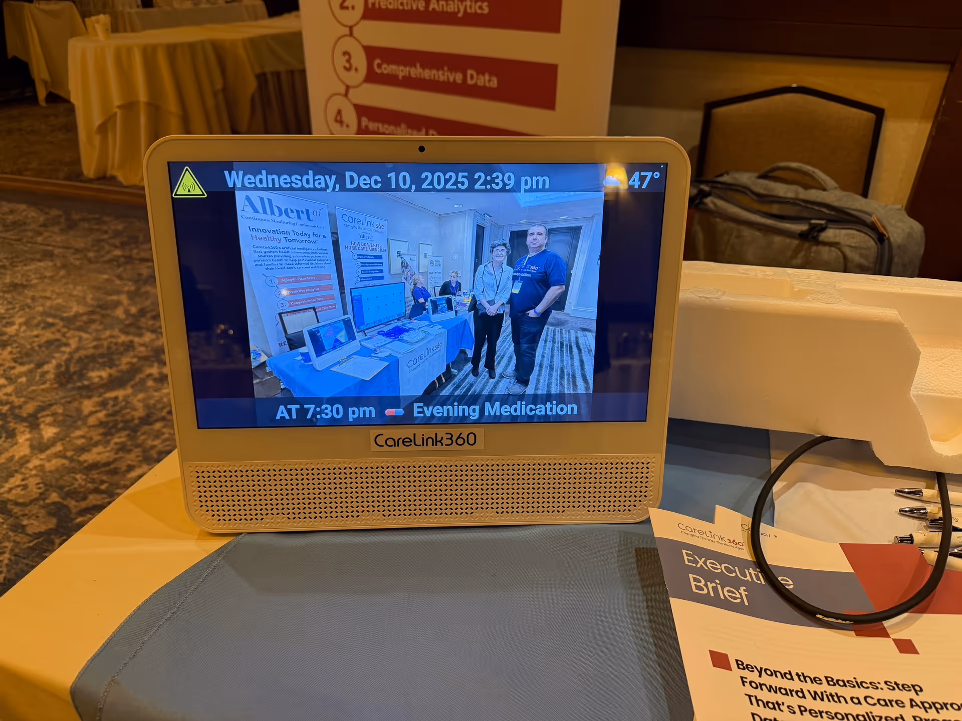 CareLink360 monitor on conference table displaying booth with two people inside screen.