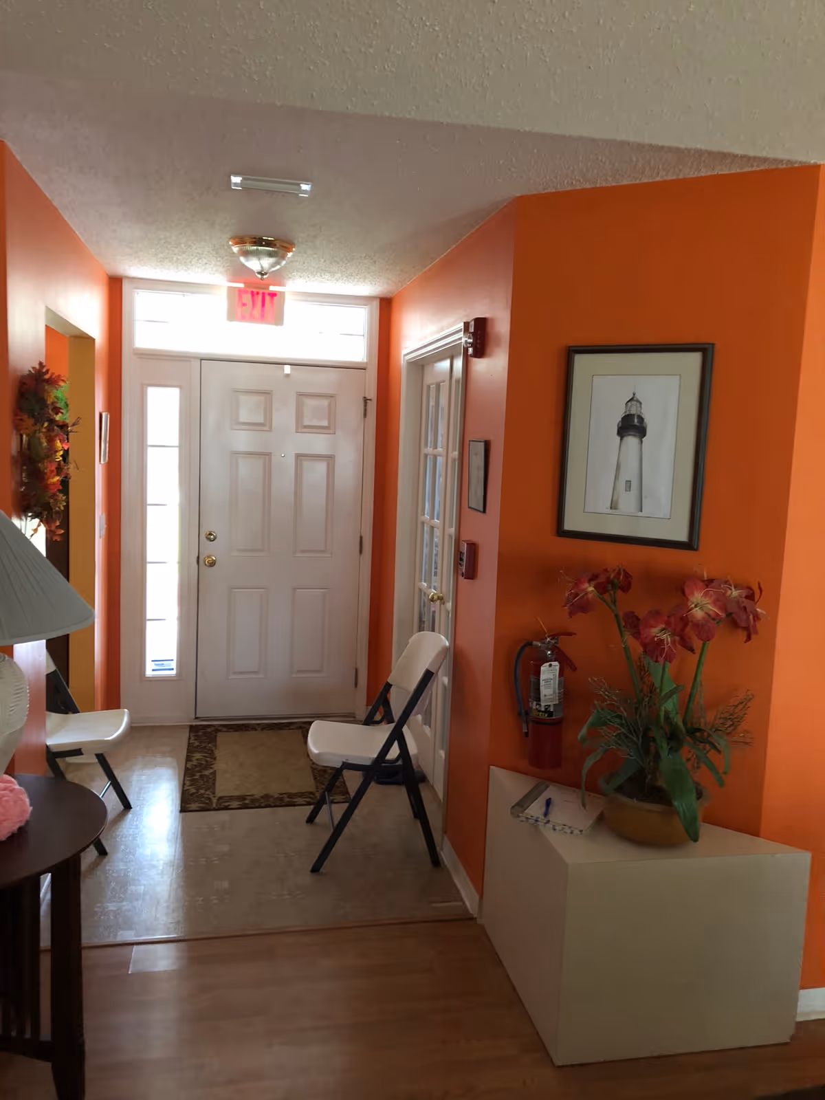 Bright orange hallway near an entry door with plants, seating, and lighthouse photo.