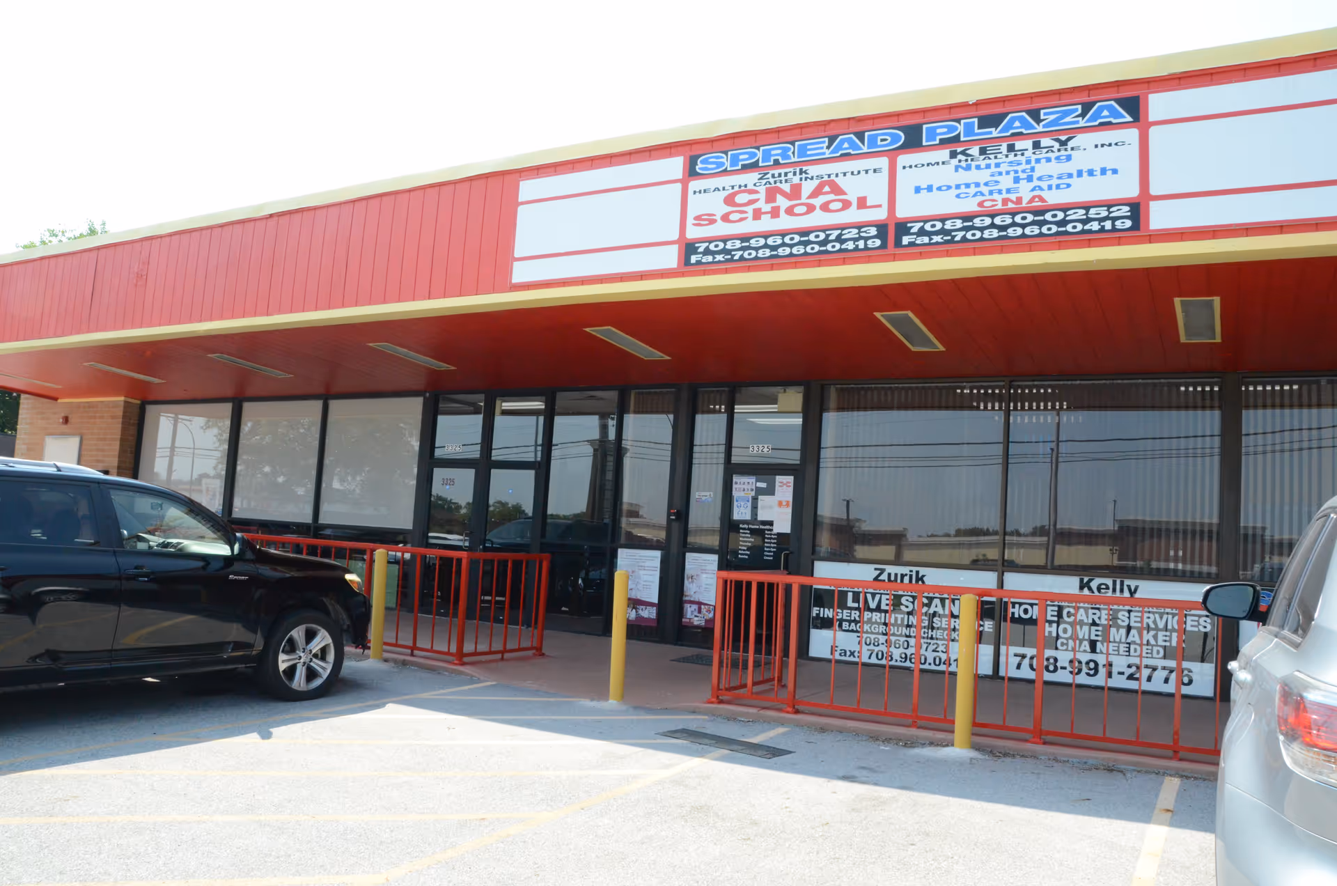 Exterior of a red storefront with large glass windows and parked cars.