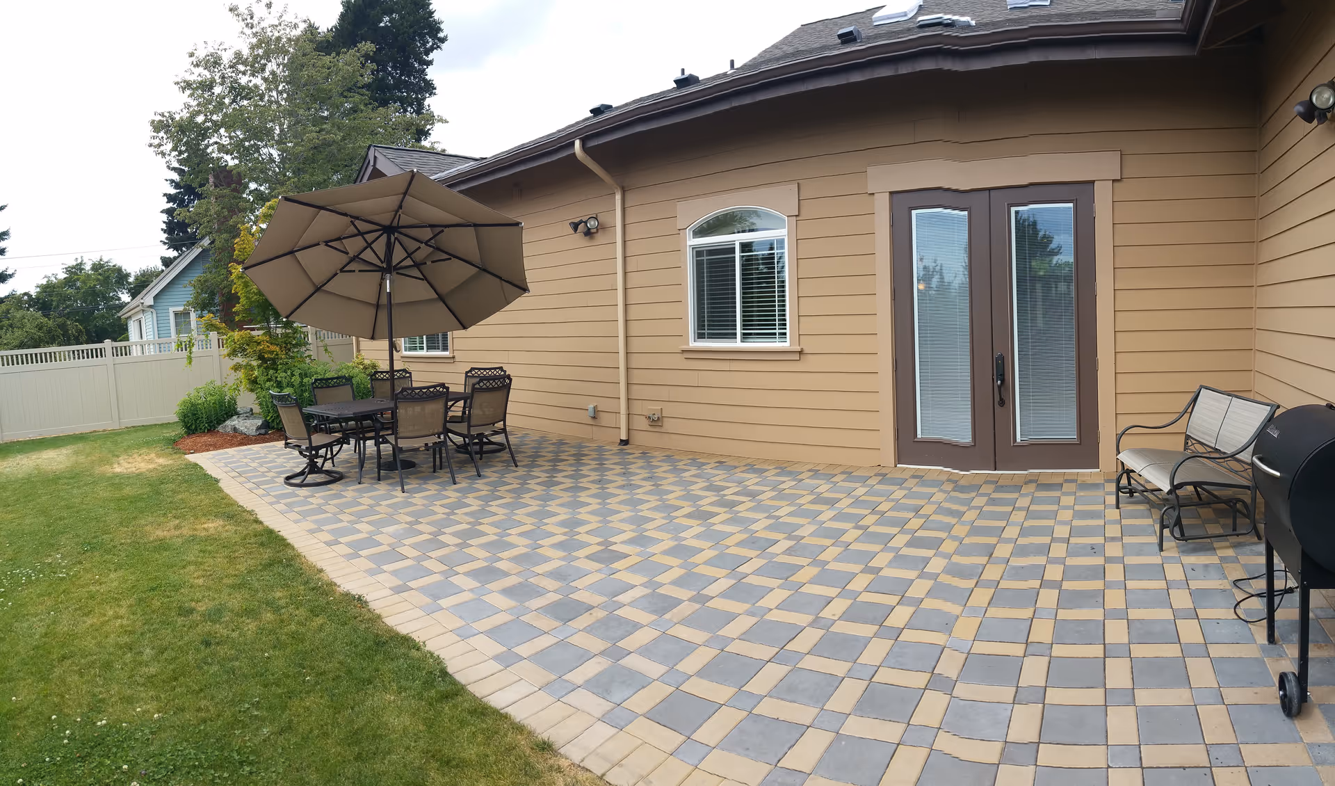Outdoor patio beside a beige building with a dining table, chairs, and a large umbrella.