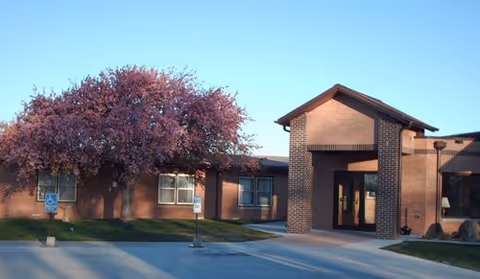Exterior view of a brick senior living facility with a front entrance and flowering trees.
