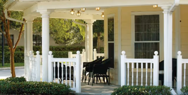 White porch with columns and outdoor seating in front of a light-colored house.
