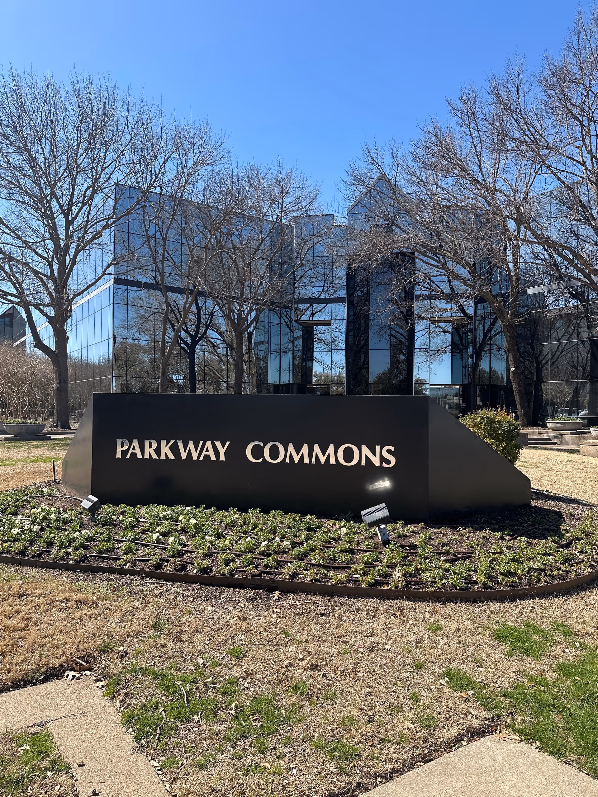 Glass-front building behind leafless trees with a black Parkway Commons sign.
