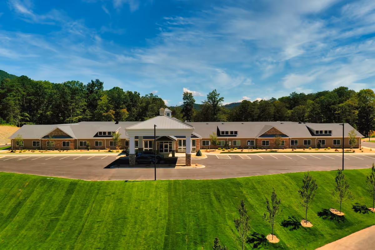 A single-story senior living facility exterior with a porte-cochère, parking, and manicured lawn.
