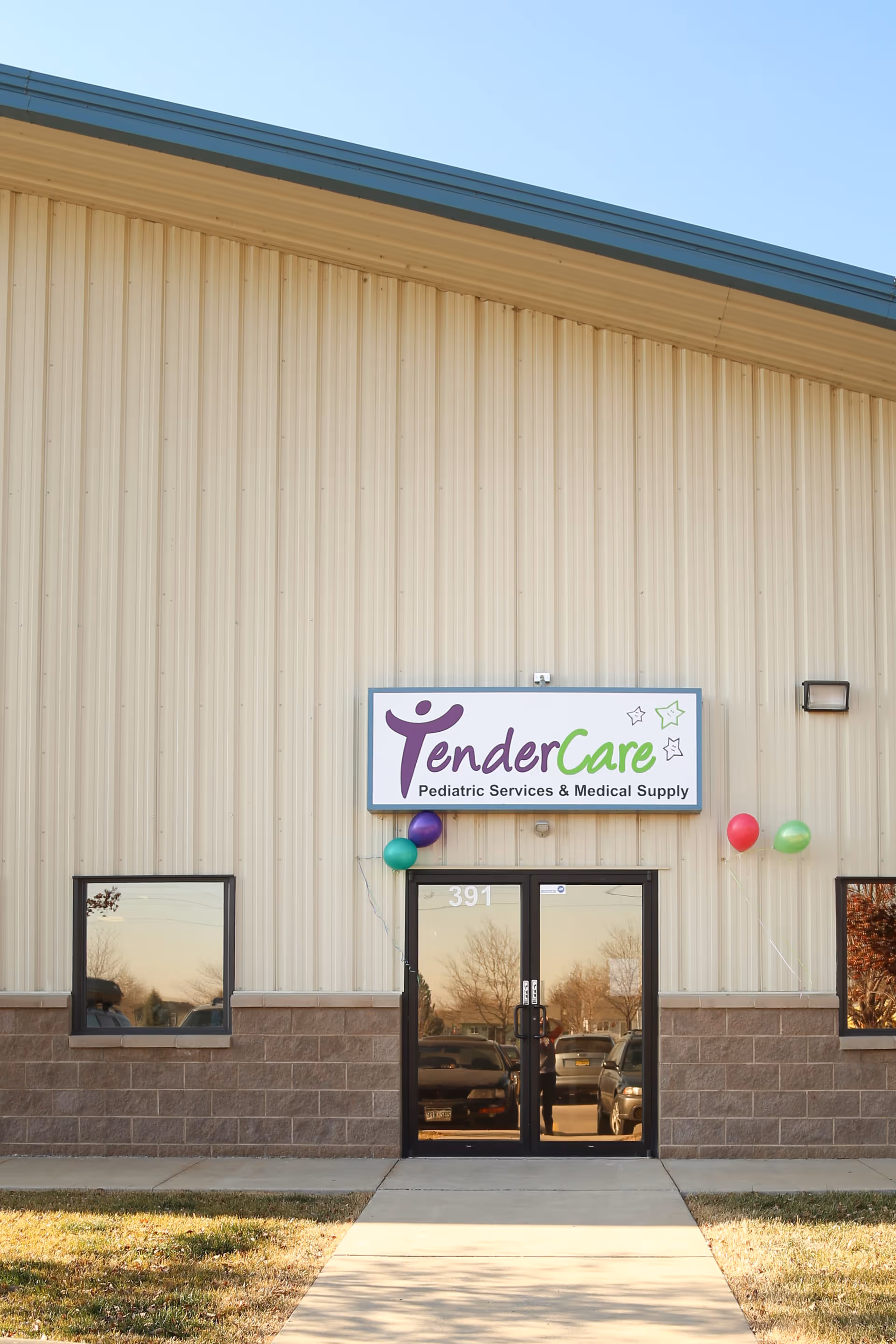 Exterior view of TenderCare entrance with sign, balloons, and glass doors.