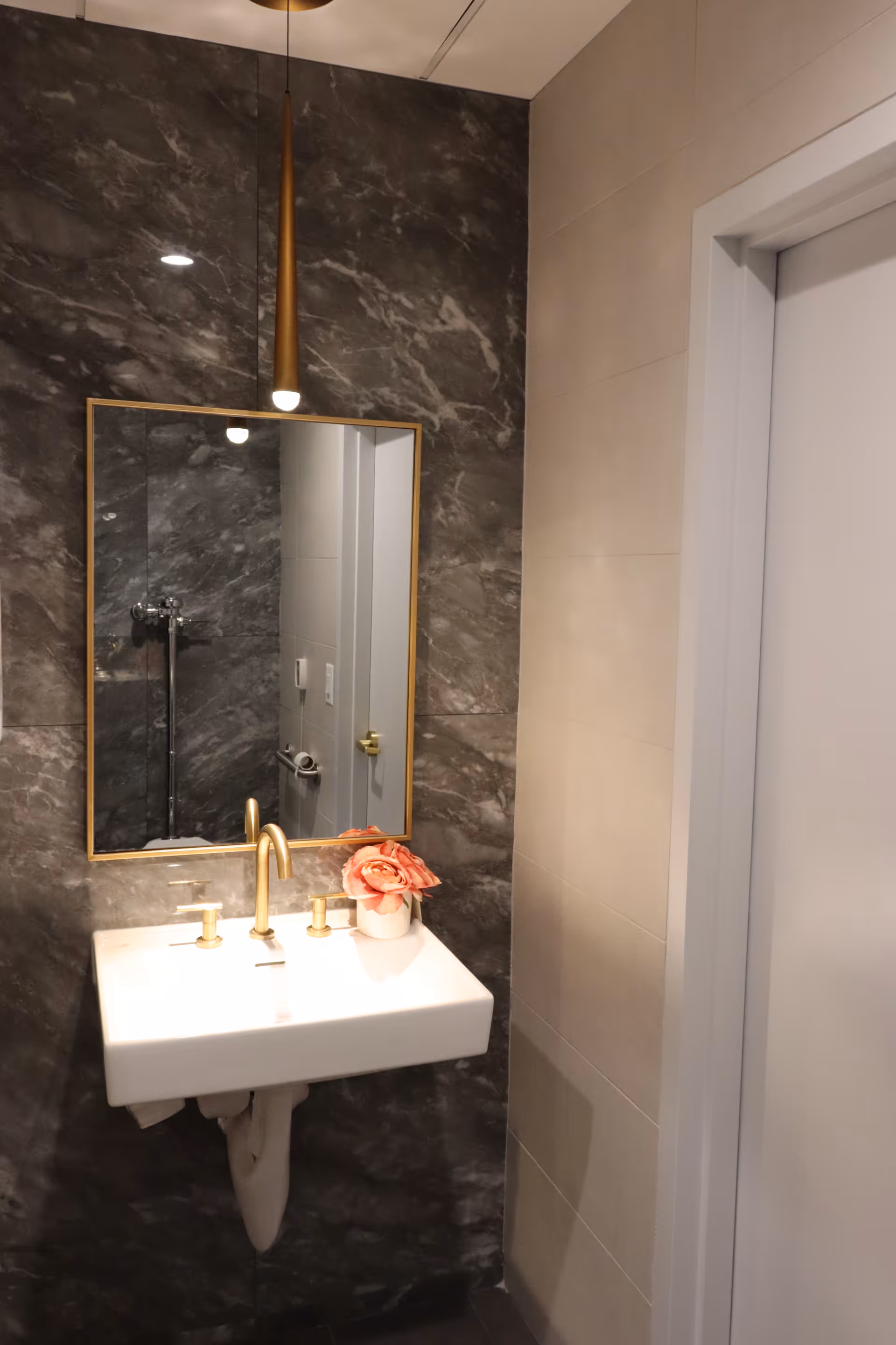 Modern bathroom with marble wall, white sink, and brass fixtures.
