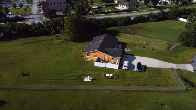 Aerial view of an orange building with driveway and expansive green lawn.